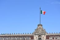 Mexican flag on historic building in Mexico City against clear blue sky.