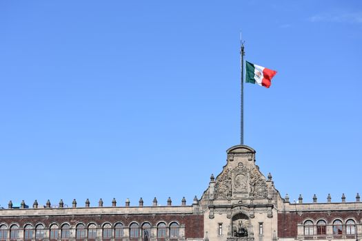 Mexican flag on historic building in Mexico City against clear blue sky.