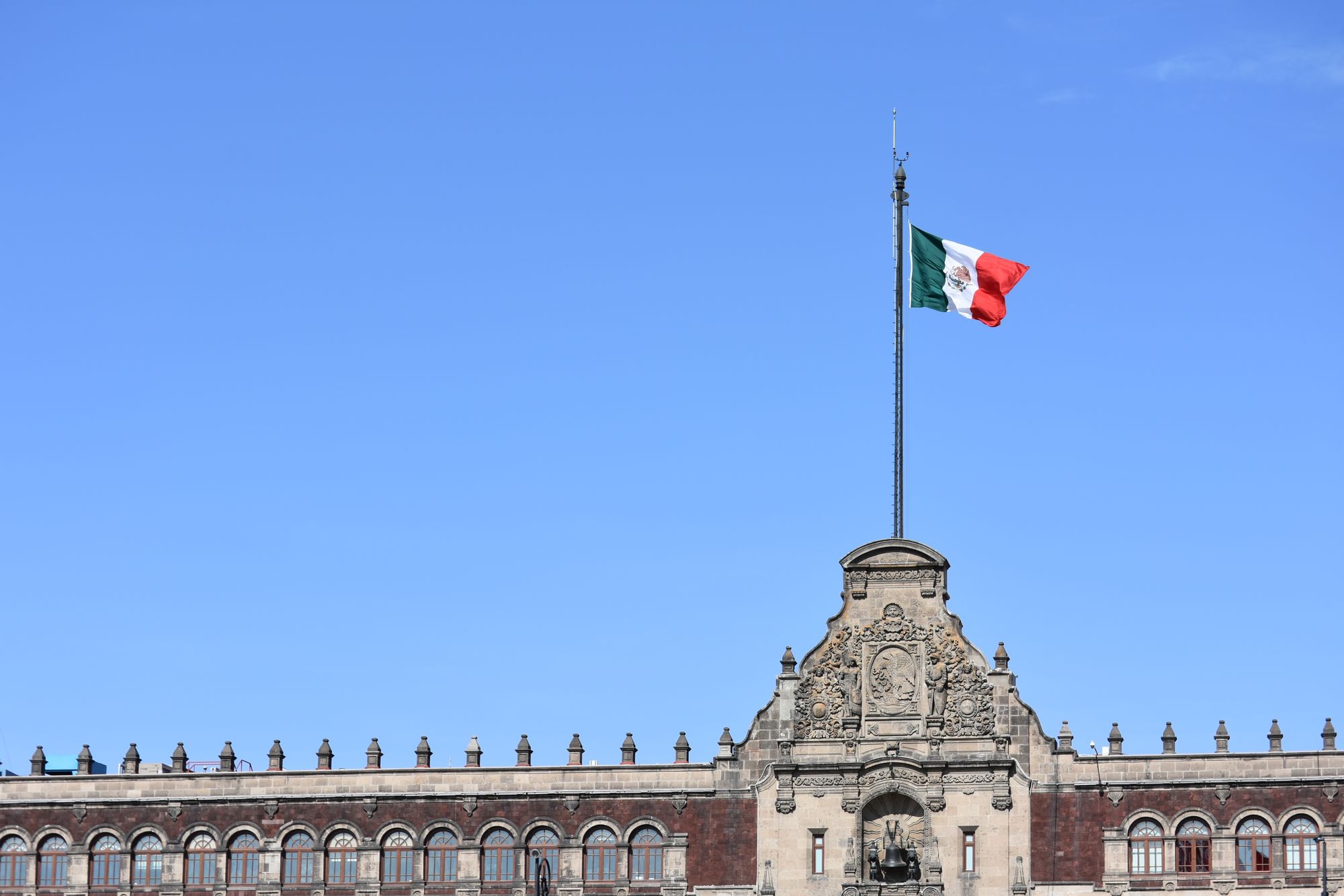 Mexican flag on historic building in Mexico City against clear blue sky.