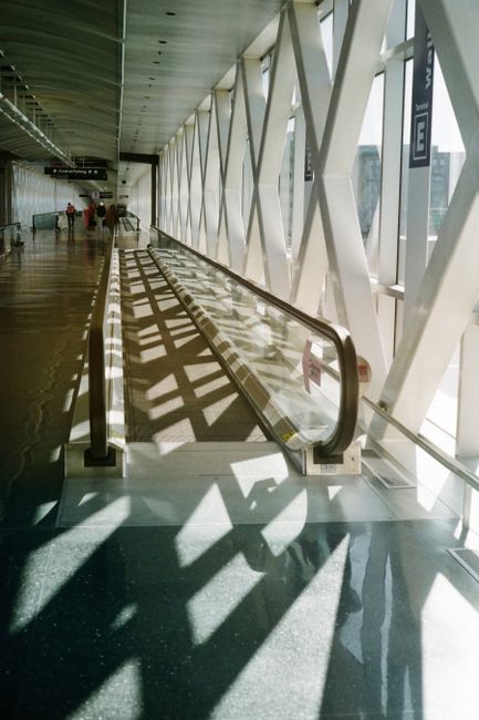 Bright airport corridor featuring a moving walkway and geometric architecture.
