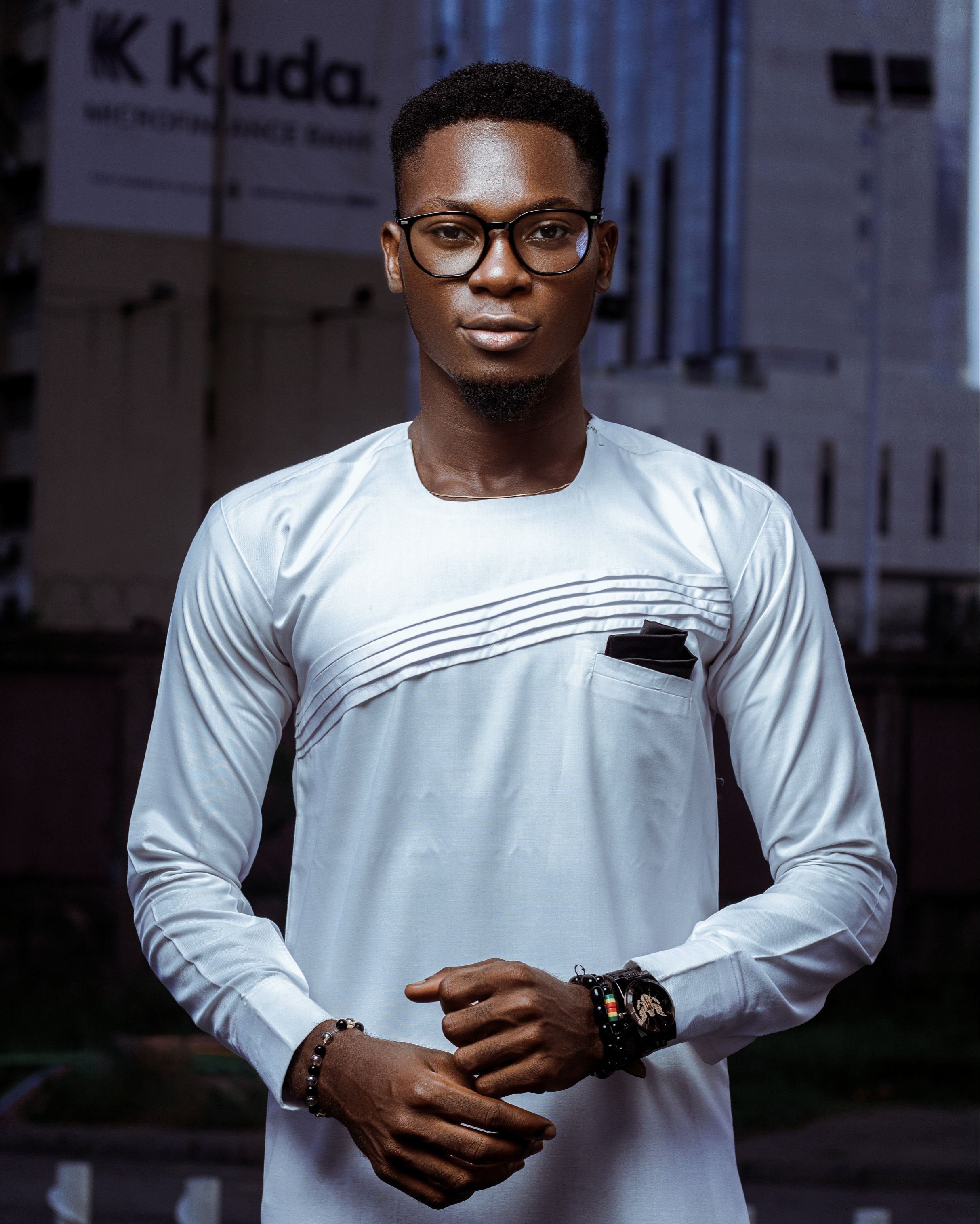 Elegant pose of a man in white attire with eyeglasses, captured in Lagos, Nigeria urban setting.