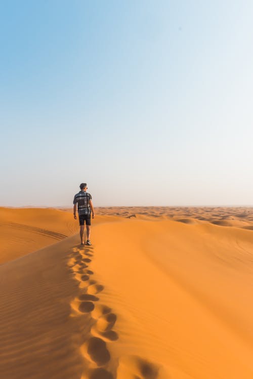 Man Walking in a Desert Under a Blue Sky