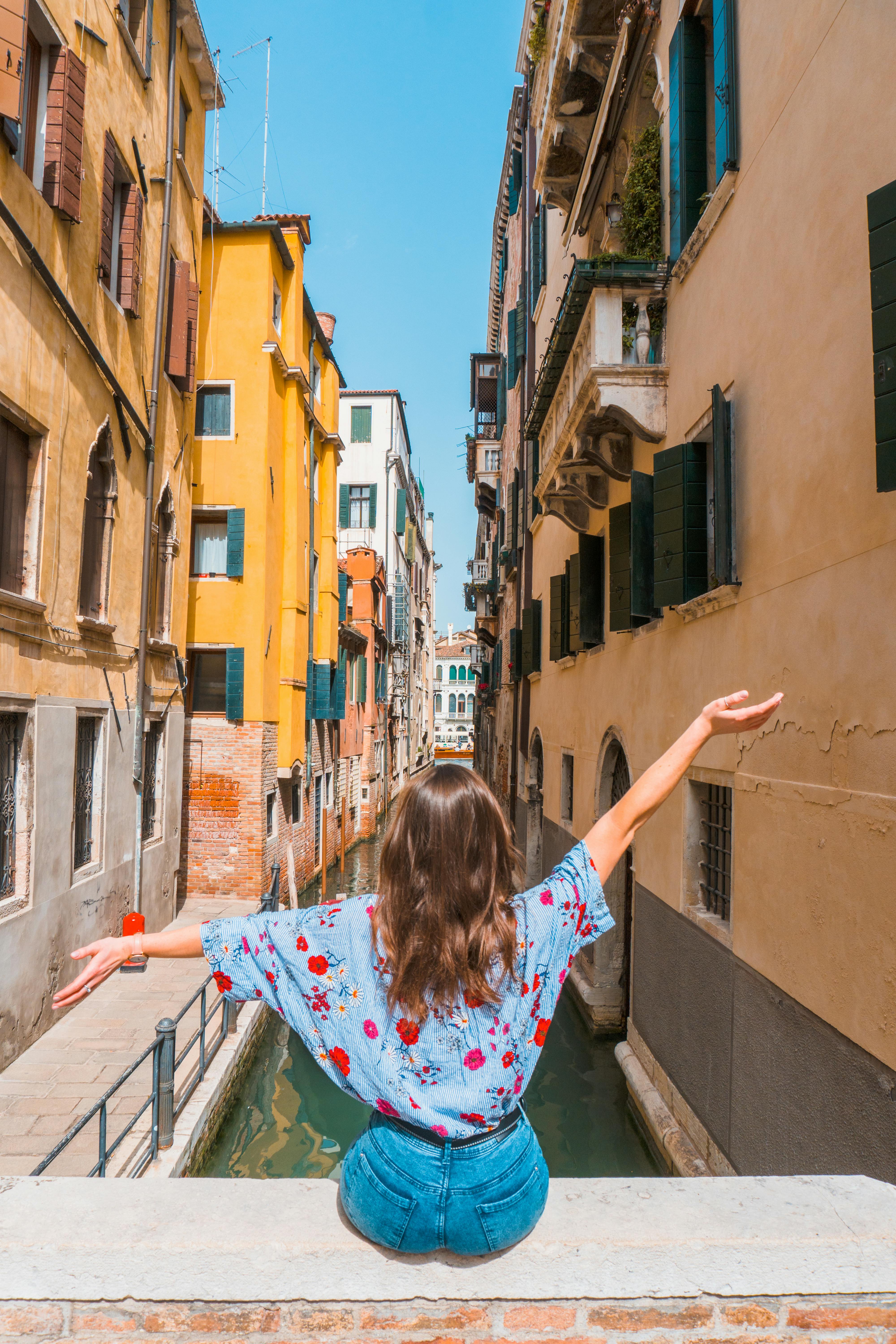 Woman enjoys serene moment sitting by a Venice canal with arms outstretched.