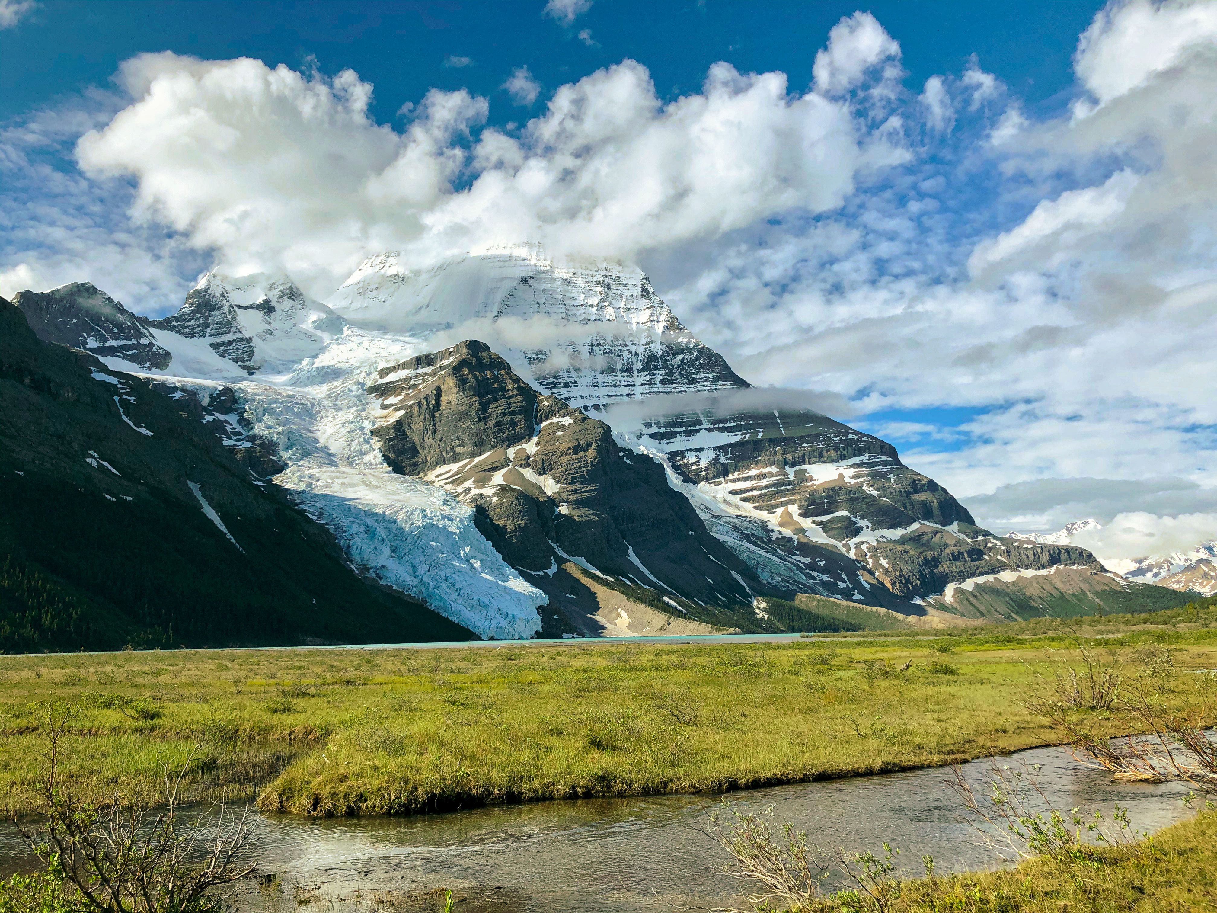 Stunning snowcapped mountain with lush meadow and cloudy sky, perfect for landscape lovers.