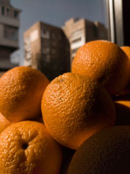 Close-up of fresh organic oranges by a window with city buildings in the background.