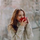 一位年轻女子穿着舒适的毛衣，在户外喝着咖啡，显得温暖而放松