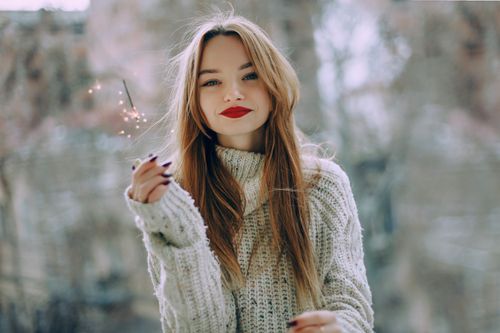 Free Portrait of a young woman with long hair and red lips holding a sparkler outdoors in Baku. Stock Photo
