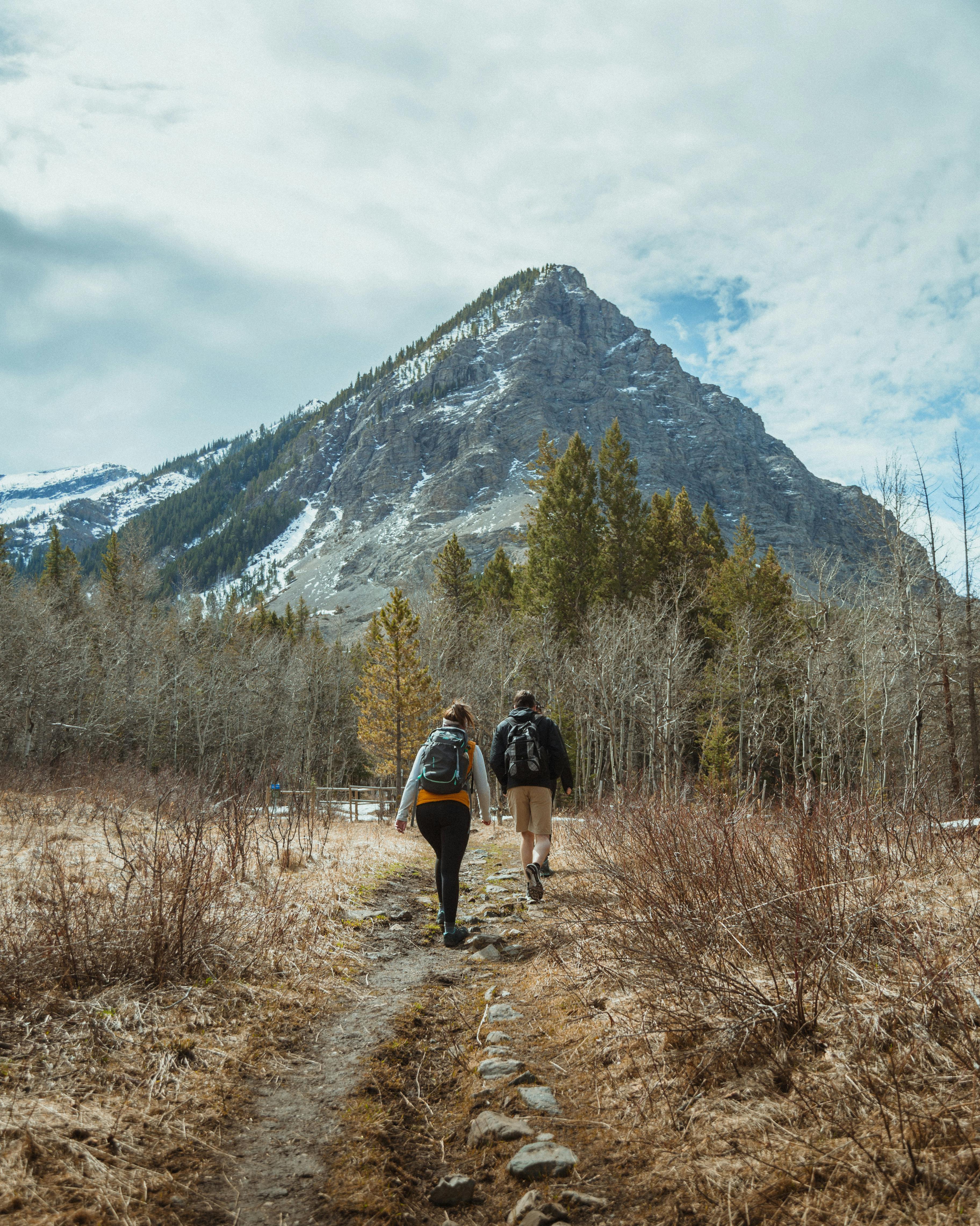 Two People with Backpacks Walking on Pathway Near Mountain · Free