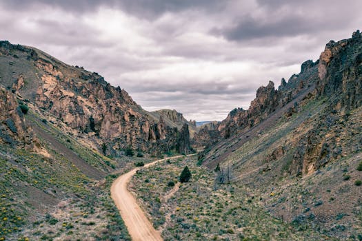 Picturesque scenery of empty narrow roadway running through green rocky mountains under cloudy sky in daytime