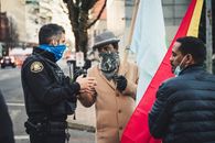Side view of concentrated policeman in uniform standing and talking with African American men in protective mask and casual clothes on city street in daytime