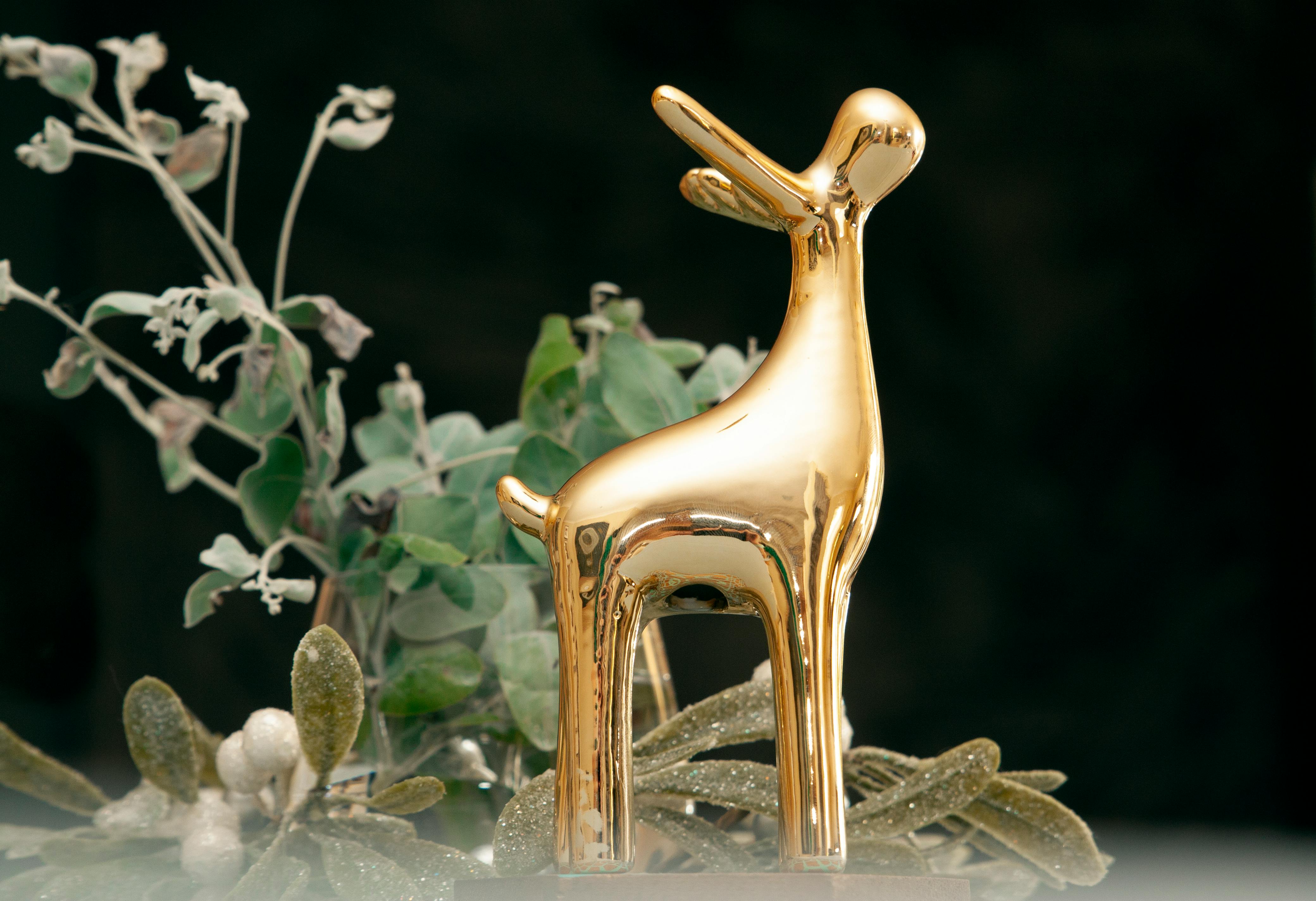 A shining golden reindeer figurine surrounded by elegant greenery, perfect for sophisticated Christmas decoration.
