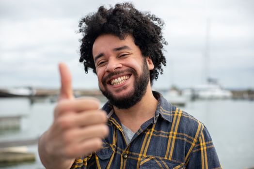 Happy man with a thumbs up gesture by the marina, expressing satisfaction and positivity.