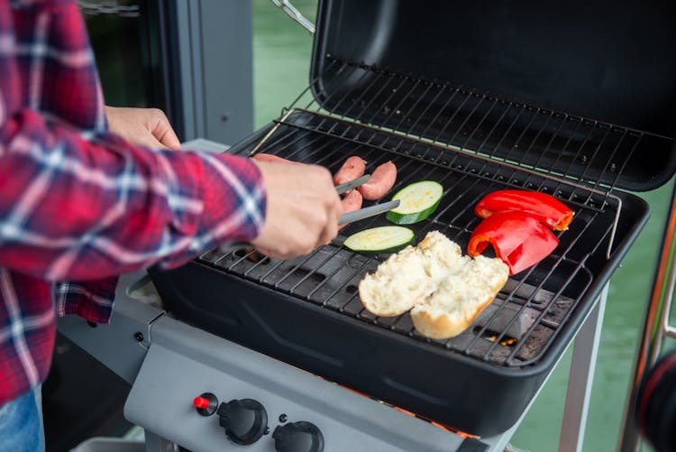 Person Grilling Sausages And Bread With Vegetables