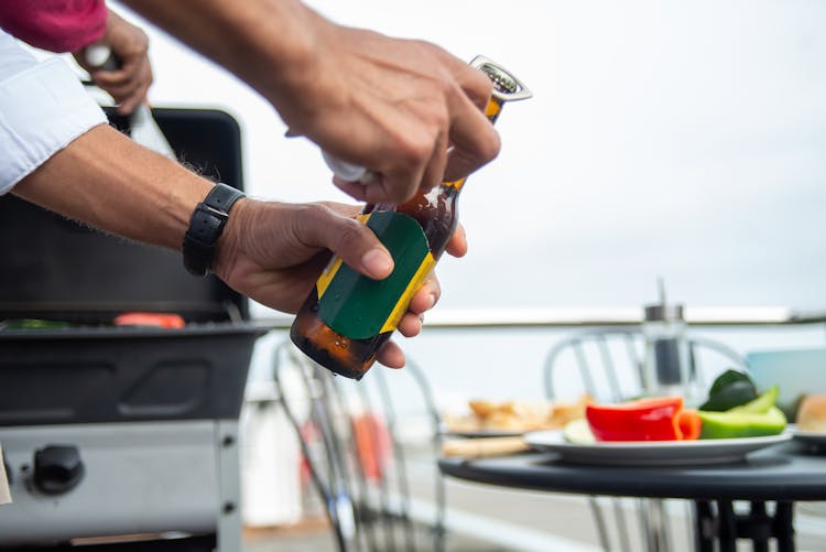 Person's Hands Opening A Brown Beer Bottle