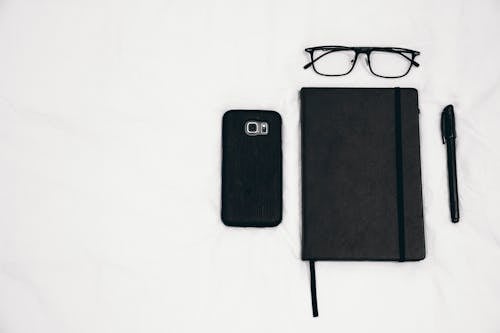 Free Black Smartphone Beside Planner and Eyeglasses and Pen Stock Photo