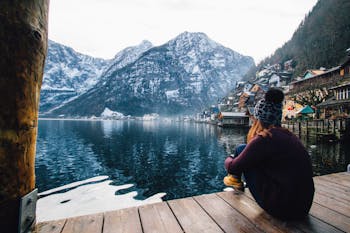 Woman in Purple Sweater Sitting on Wooden Floor With View of Lake and Mountains