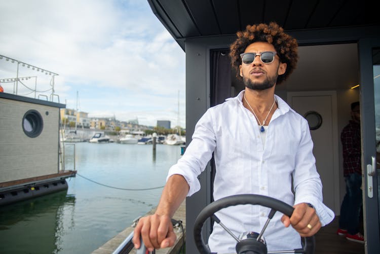 A Man In White Long Sleeves Driving A Yacht While Holding A Helm