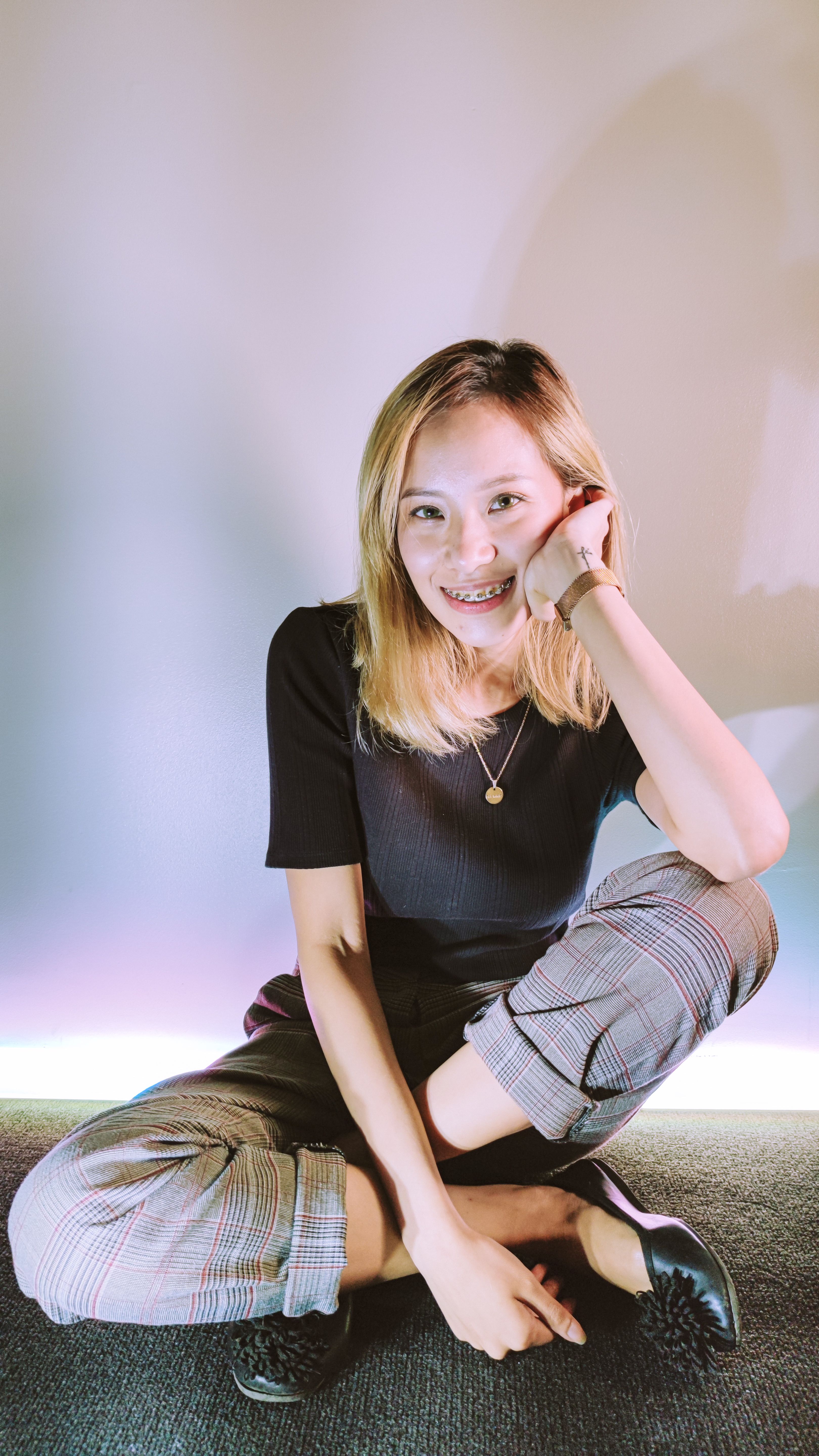 A cheerful young woman with braces smiling while sitting cross-legged, wearing a fashionable outfit.