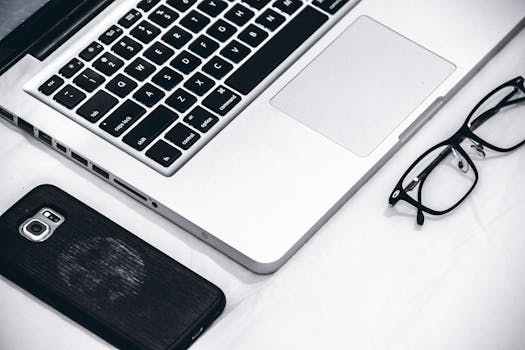 Close-up of a modern workspace featuring a laptop, smartphone, and glasses on a desk.