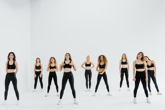 A diverse group of women in sportswear performing a dance routine in a bright studio setting.