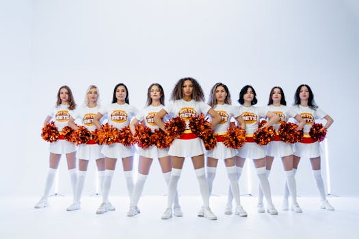 Cheerleading team posing with orange pompoms on white backdrop, showcasing team spirit.