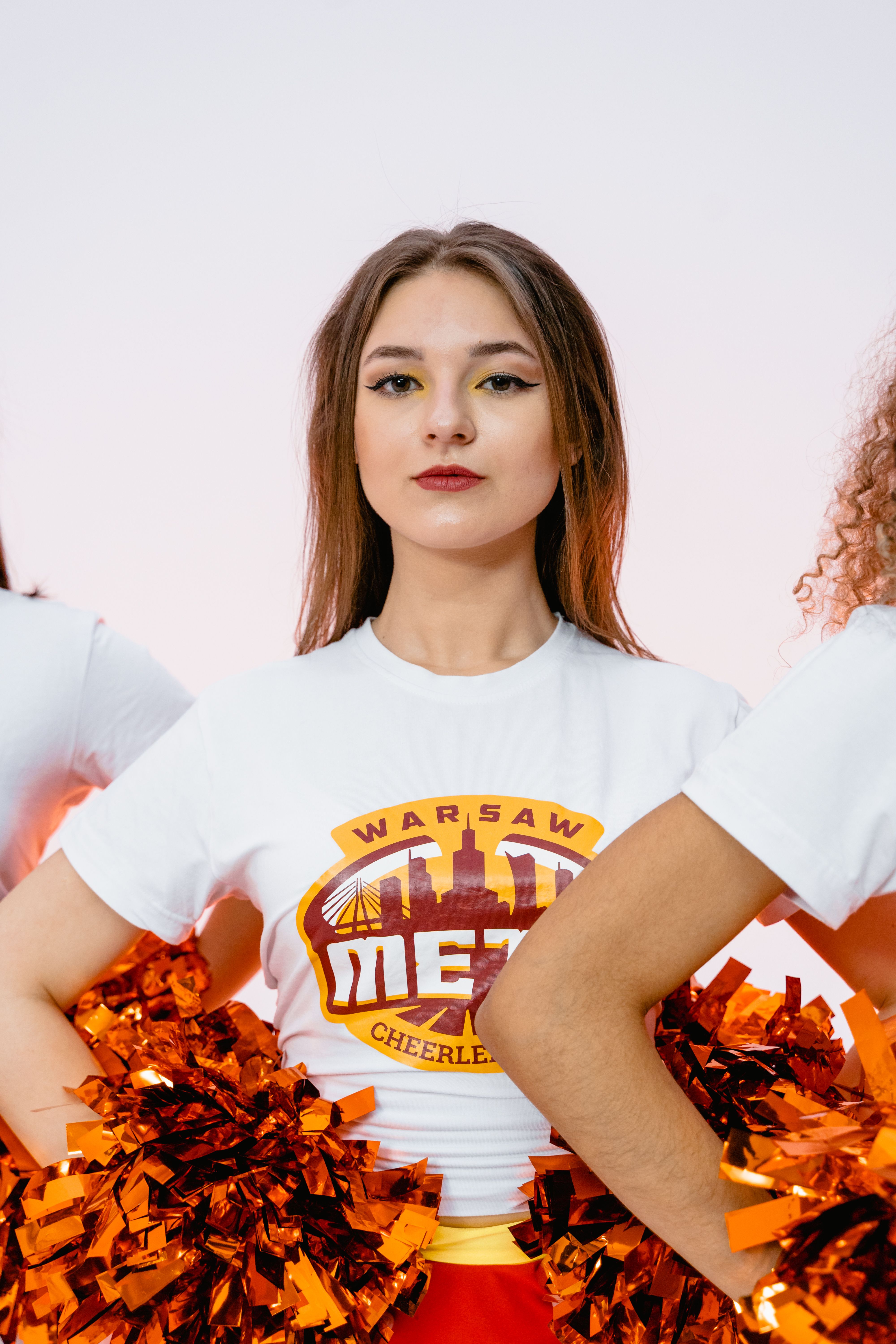 Young woman cheerleader posing confidently with red pom poms and stylish makeup.
