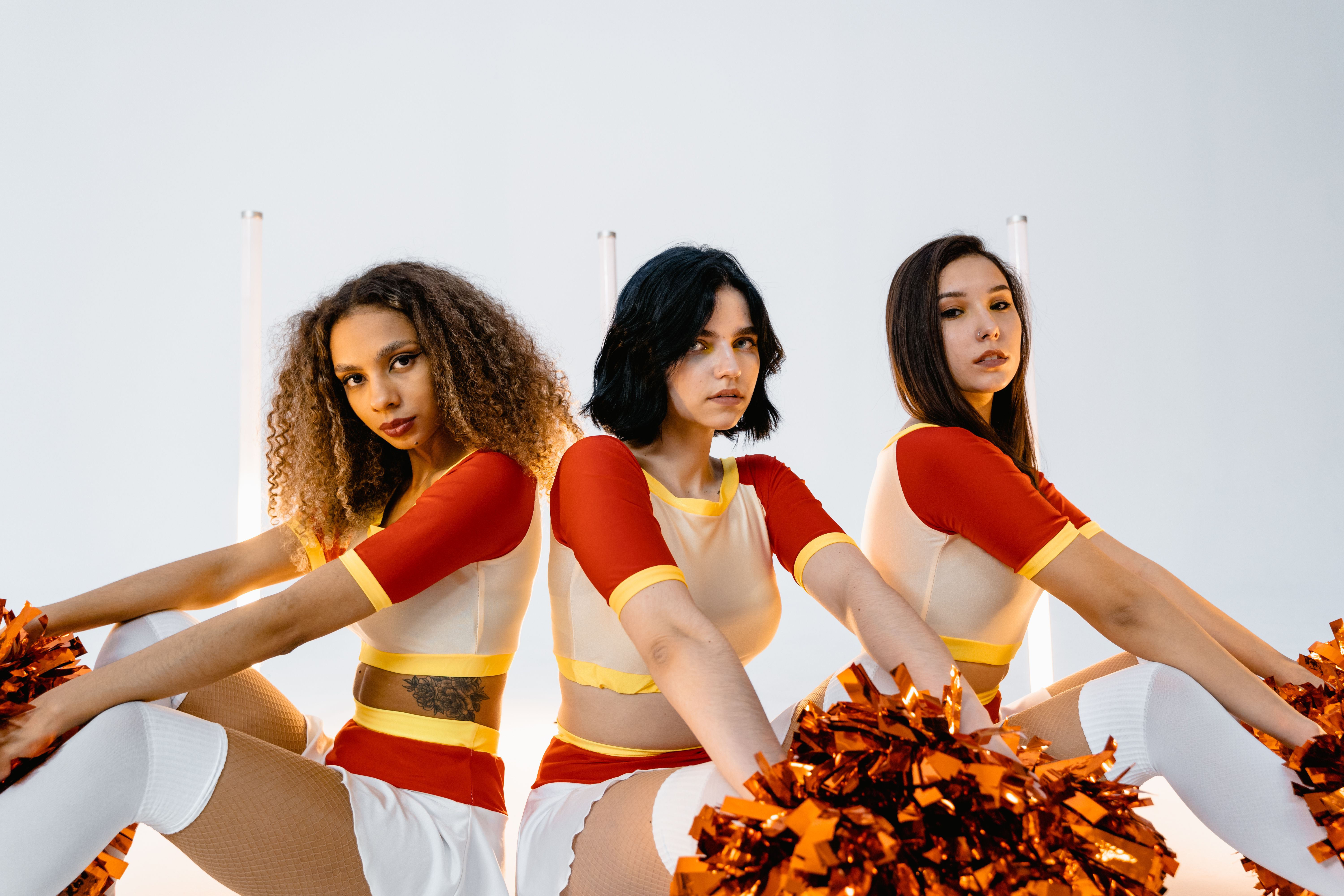 Energetic portrait of three diverse cheerleaders in vibrant uniforms holding pom poms indoors.