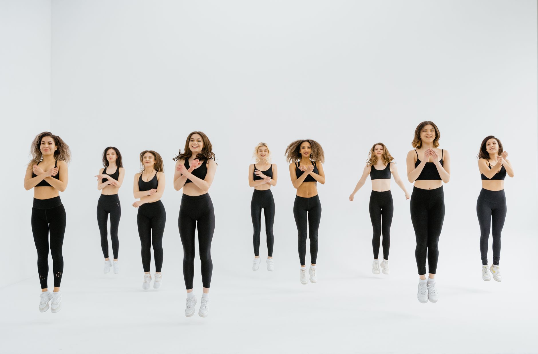 Nine women in activewear jumping energetically in a fitness class indoors.