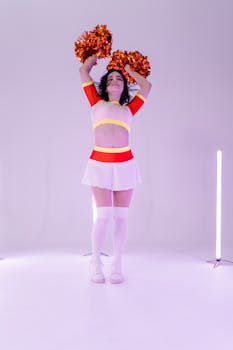 Energetic cheerleader in uniform posing with pom poms in a bright studio setting.
