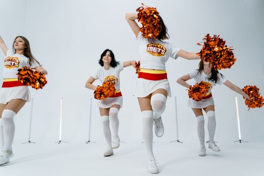 Dynamic group of cheerleaders performing with pom poms in a studio setting.