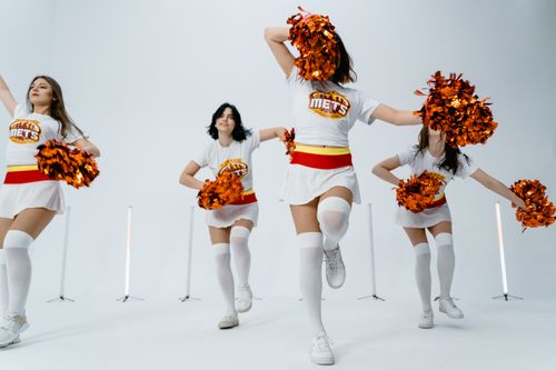 Free Dynamic group of cheerleaders performing with pom poms in a studio setting. Stock Photo