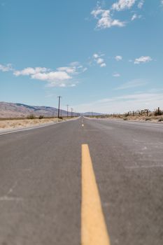 Straight desert highway under clear blue sky with scattered clouds