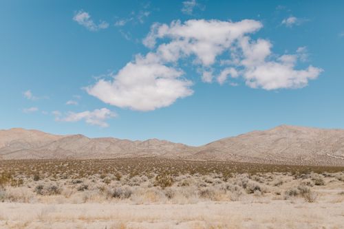 Free Vast desert landscape under a bright blue sky with scattered white clouds. Stock Photo