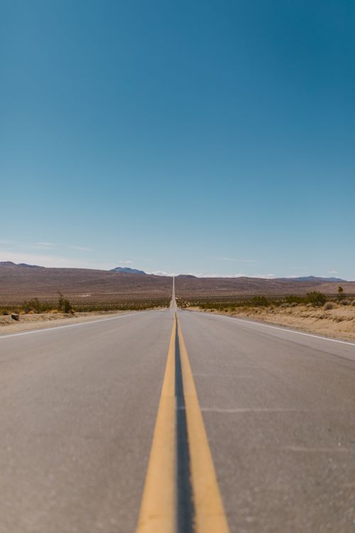 Free A straight road disappearing into the horizon under a clear blue sky. Stock Photo