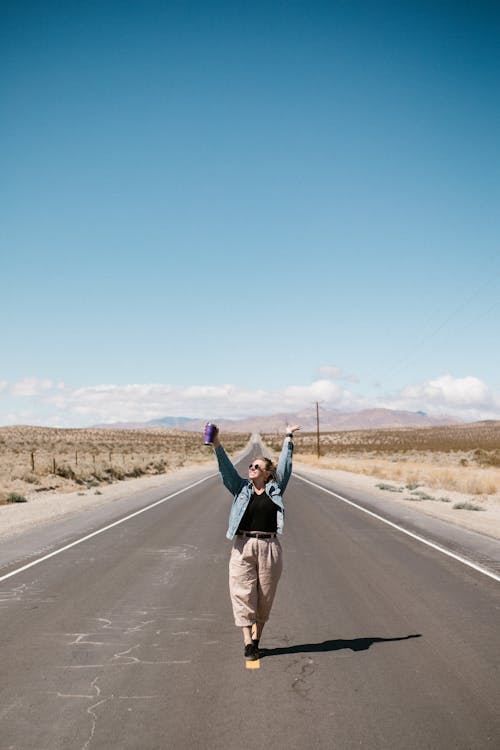A Woman in Denim Jacket and Pants in the Middle of a Long Road