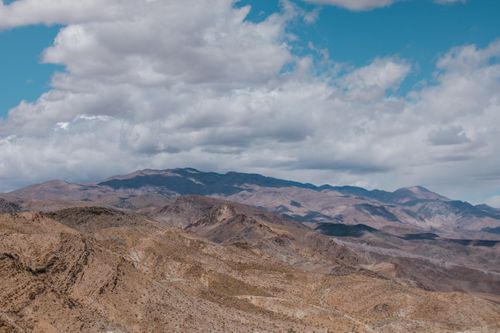Free Breathtaking panorama of the arid Death Valley desert, showcasing rugged hills and a distant mountain range under vast clouds. Stock Photo