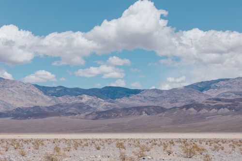 Free A stunning view of a desert with mountains under a bright blue sky and fluffy white clouds. Stock Photo