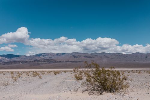 Free Expansive desert terrain under a bright blue sky with distant mountain range. Stock Photo