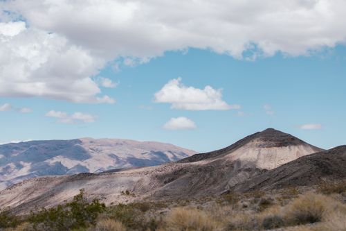 Free Breathtaking view of desert terrain with mountains under a vibrant blue sky and fluffy white clouds. Stock Photo