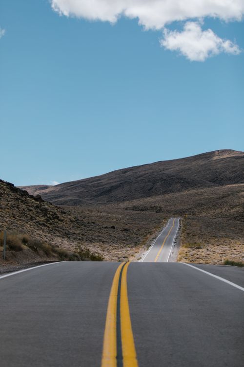 Free Straight road stretching into remote mountains under a clear blue sky. Stock Photo