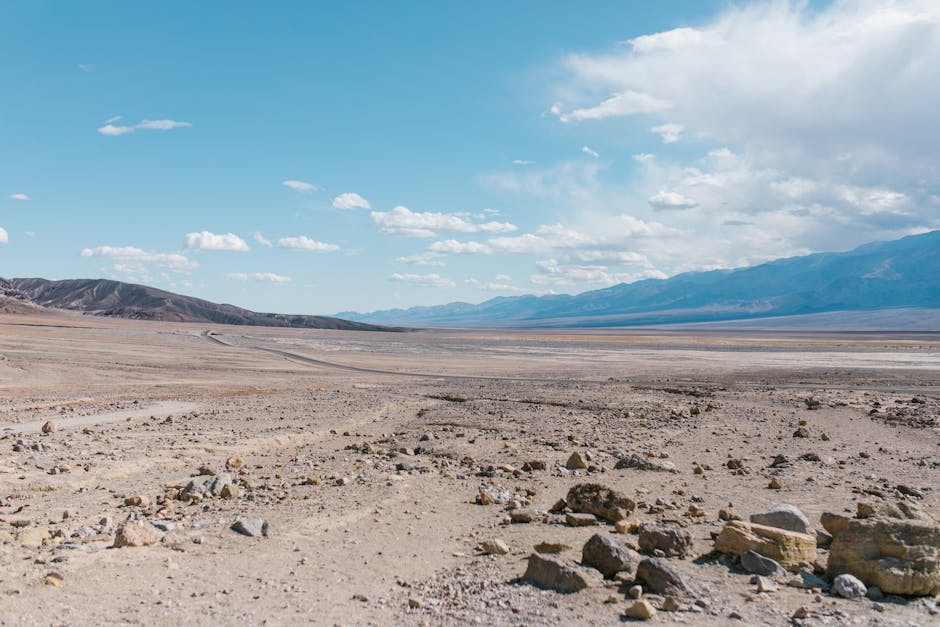 Vast desert landscape featuring rugged mountains under a bright blue sky with scattered clouds.