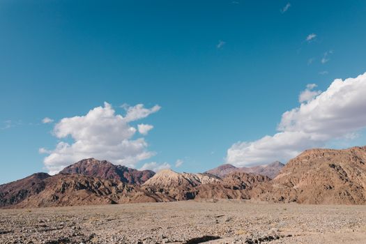 Expansive view of arid mountains and rocky terrain under a blue sky in Death Valley, California.
