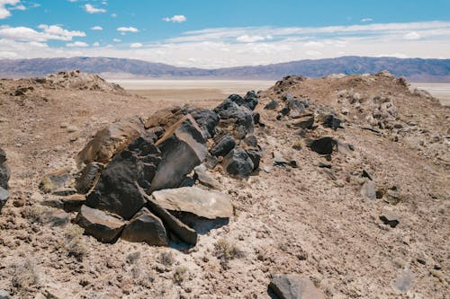 Gray and Brown Rocks on Dry Field Near Mountains Under Blue Sky
