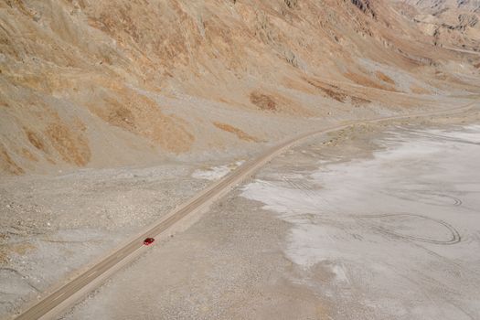 Aerial photo of a red car driving through a remote desert road, showing vast arid landscape.