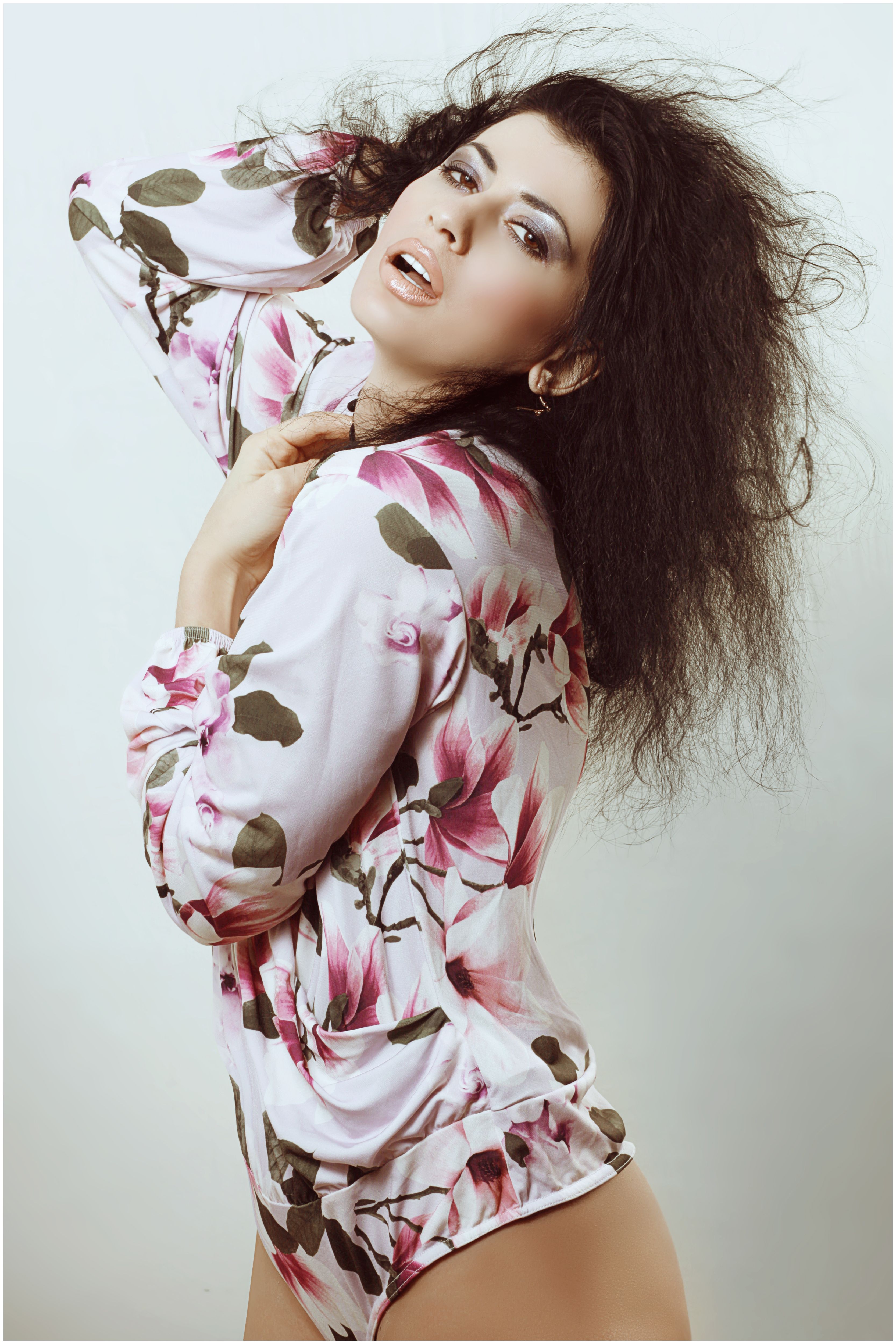 Stylish woman in floral dress strikes a confident pose indoors, showcasing modern fashion.