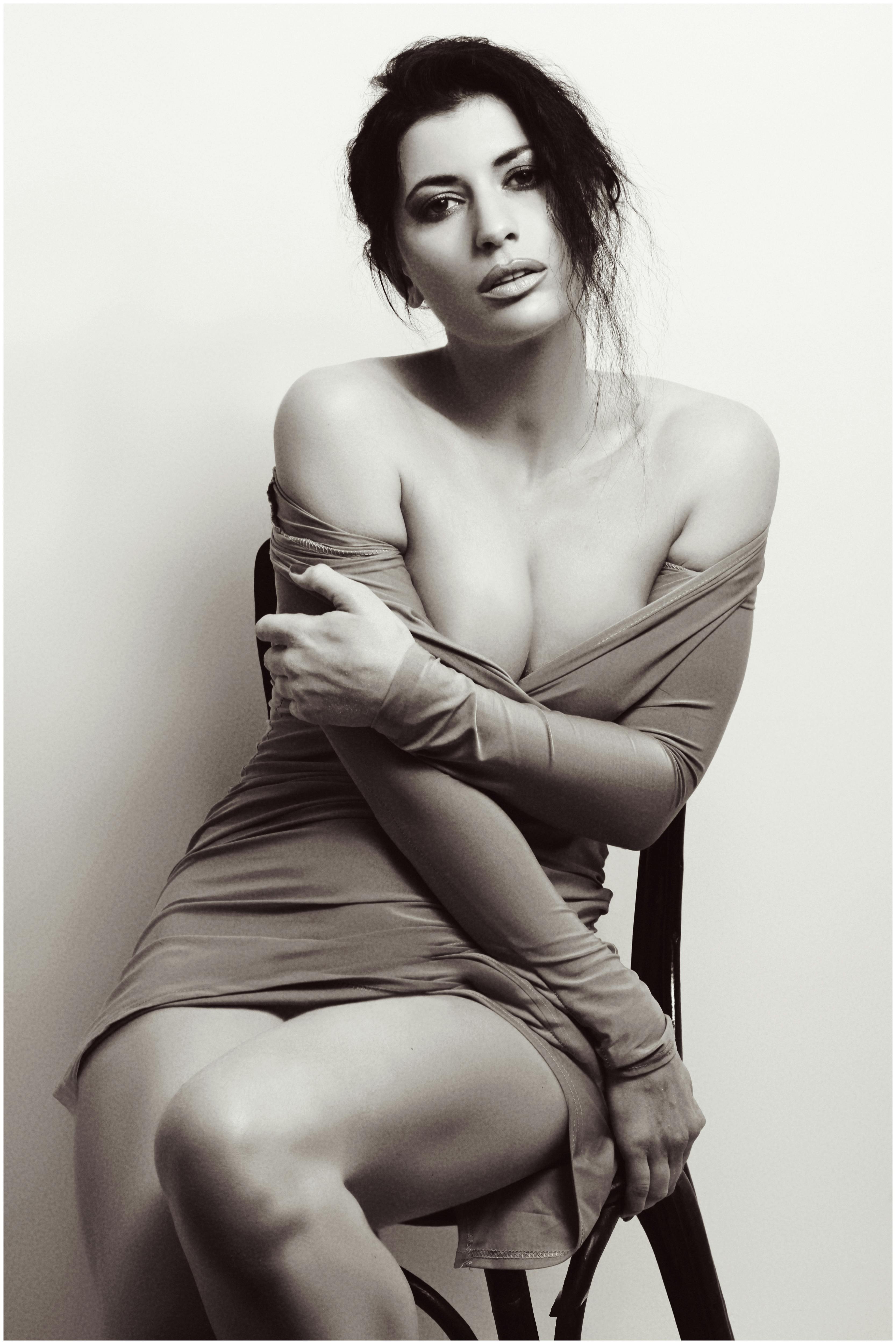 Black and white studio portrait of a woman seated in a seductive pose.