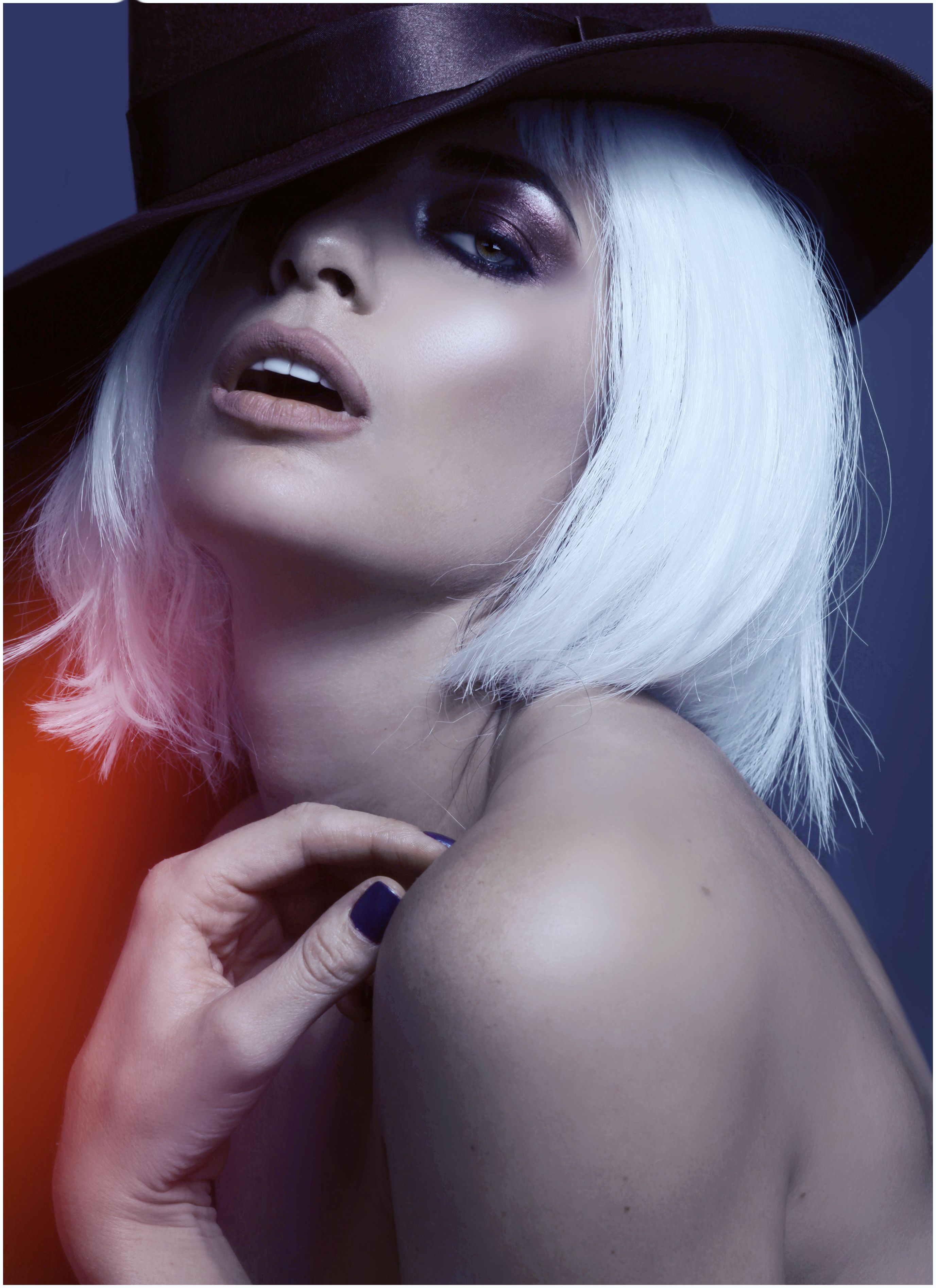 Portrait of a stylish woman with white hair and dramatic makeup wearing a hat.
