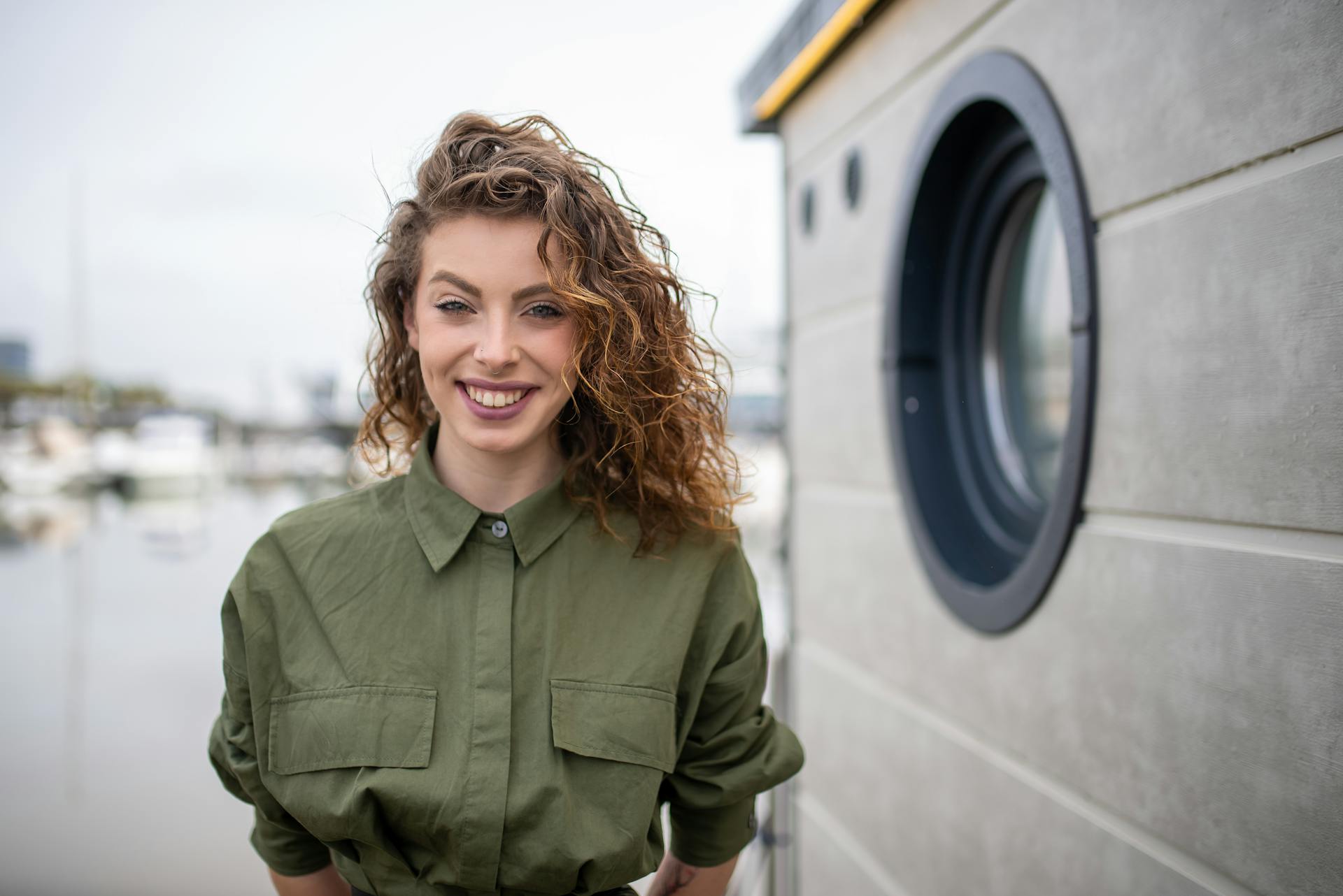 Young woman with curly hair smiling by a marina in Portugal, capturing a cheerful moment