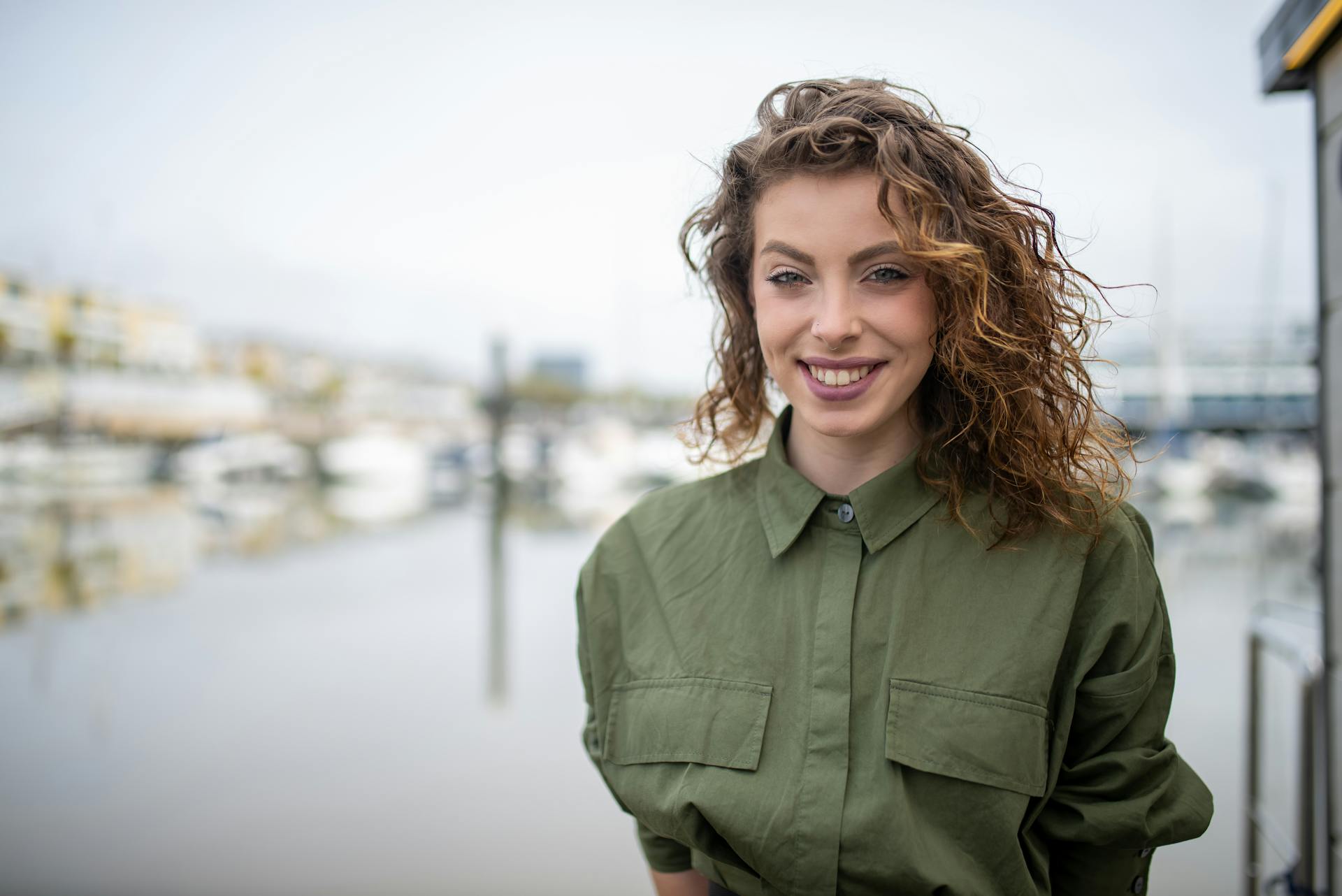 Portrait of a smiling woman with wavy hair at a marina in Portugal, wearing a green top.