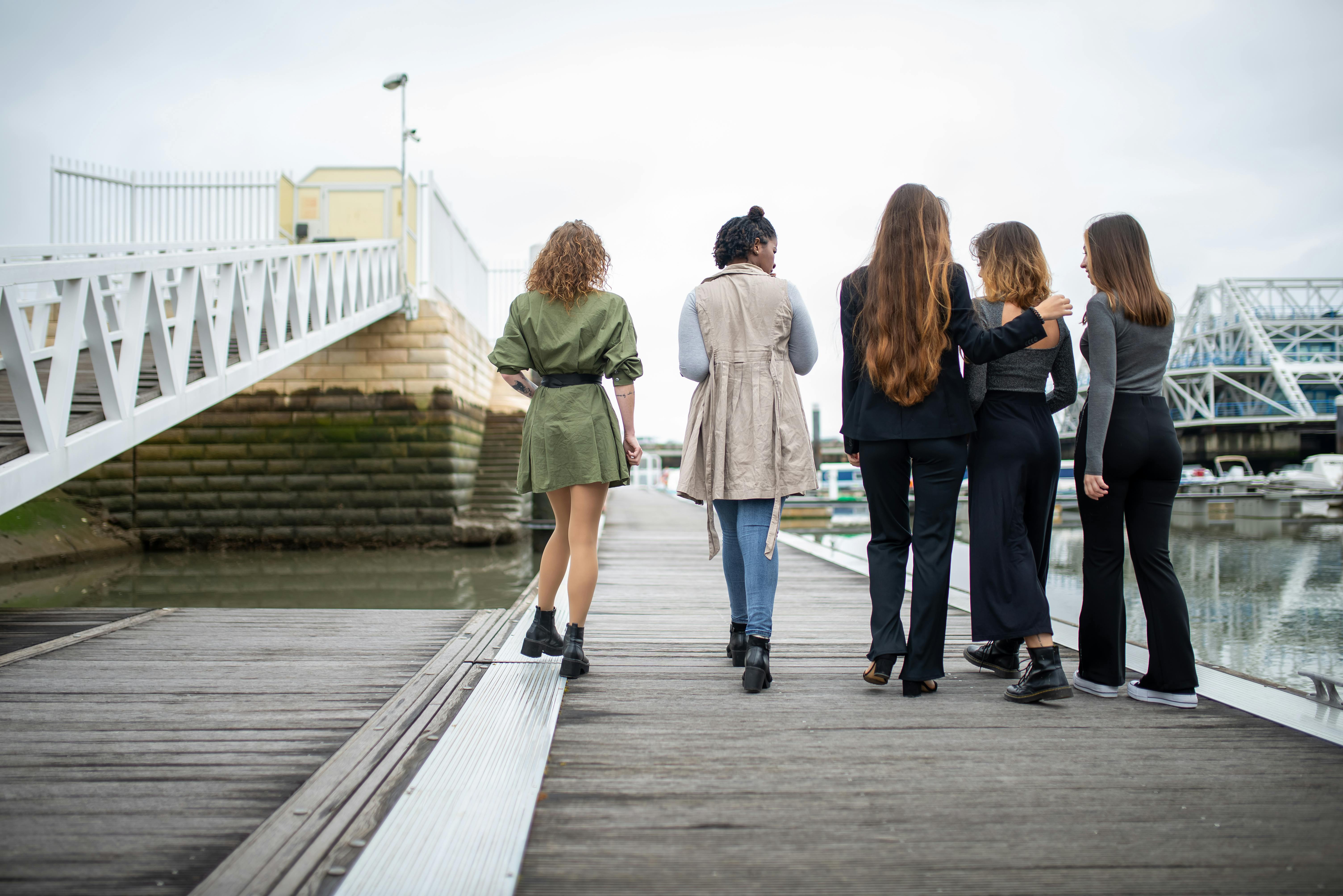 Five women walking on a wooden dock by the water in Portugal, capturing friendship and travel vibes.